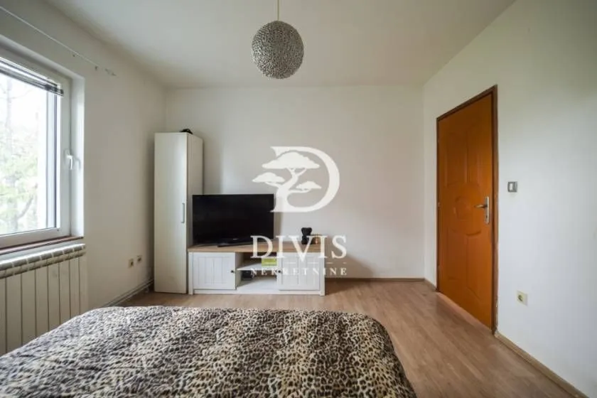 Manja spavaća soba sa krevetom, TV komodom i ormarom.