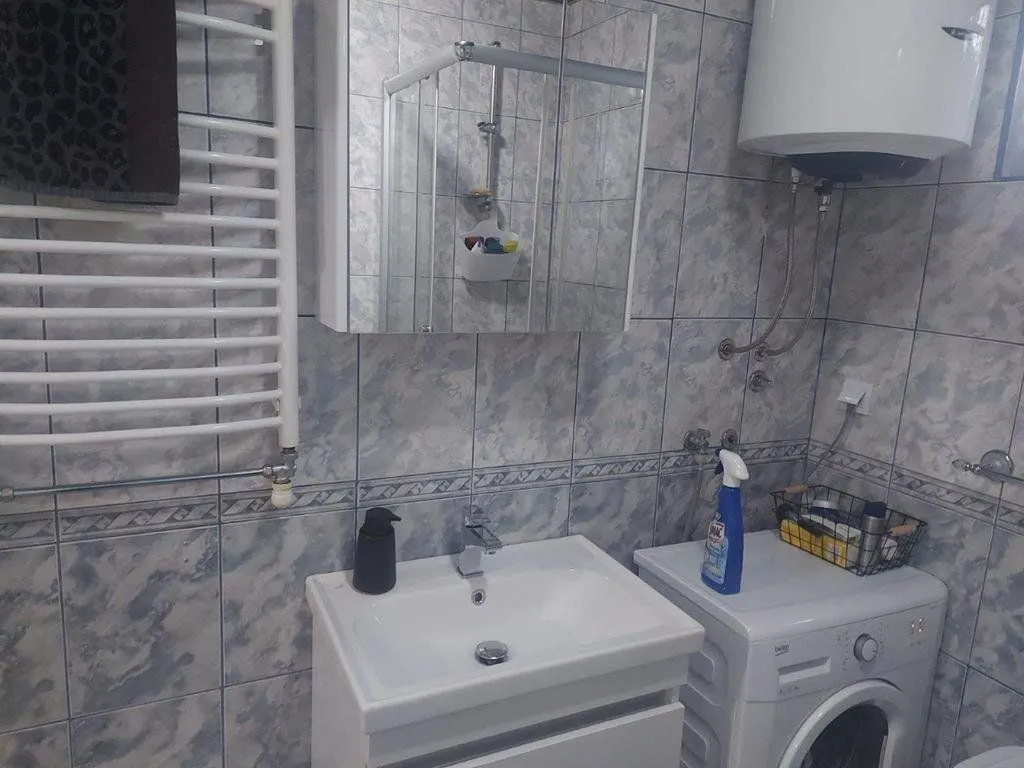 Kupatilo sa umivaonikom, veš mašinom i pločicama na zidovima.