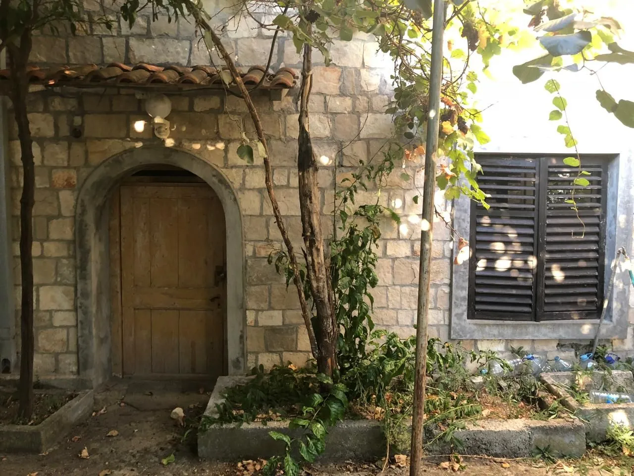 Kamena fasada stare kuće sa drvenim vratima i prozorom sa kapcima.