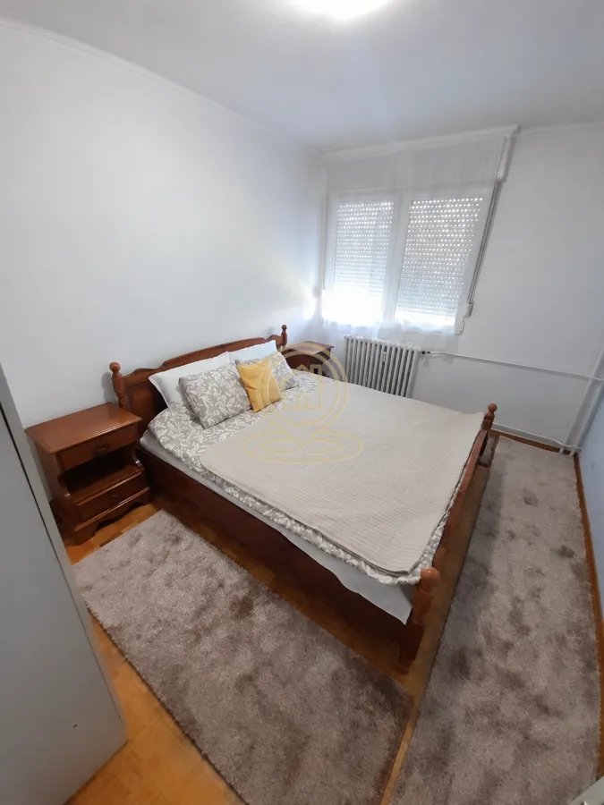 Spavaća soba sa bračnim krevetom, noćnim ormarićima i tepisima.