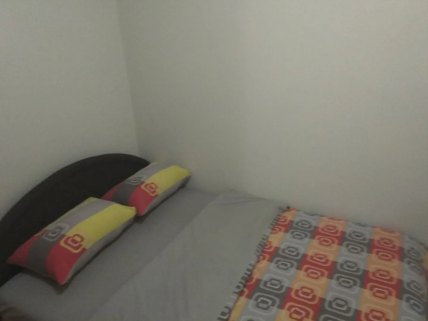 Manja spavaća soba sa krevetom i šarenim jastucima.