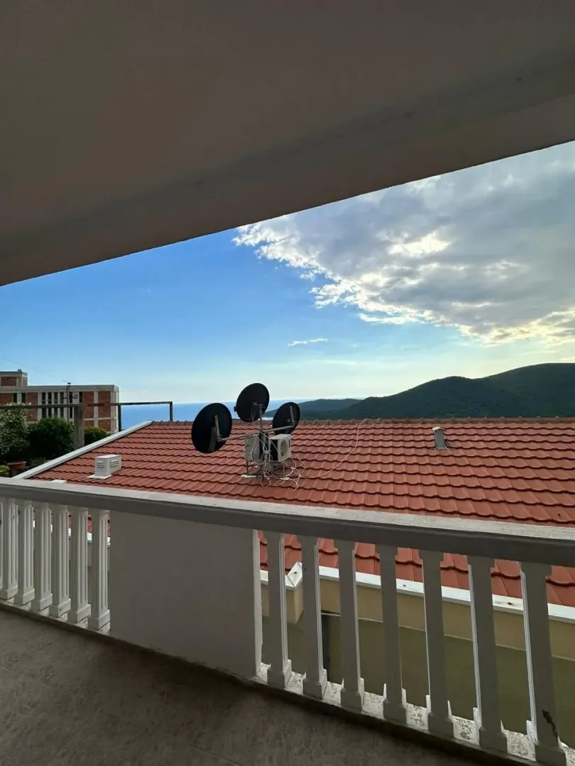 Pogled sa balkona na krovove i brda u daljini.