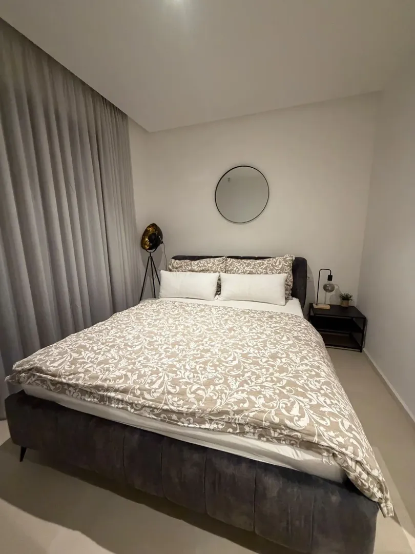 Moderna spavaća soba sa bračnim krevetom, draperijama i ogledalom na zidu.