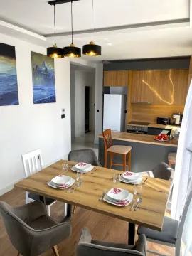 Dining area with a wooden table and chairs, connected to the kitchen in the background. - image 9