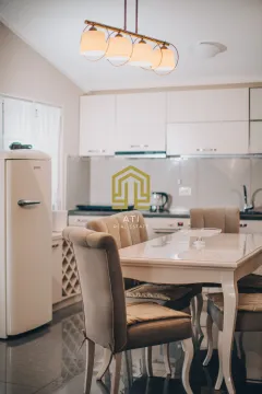 Trpezarija povezana sa kuhinjom sa svijetlim namještajem i modernim lusterom. - image 6