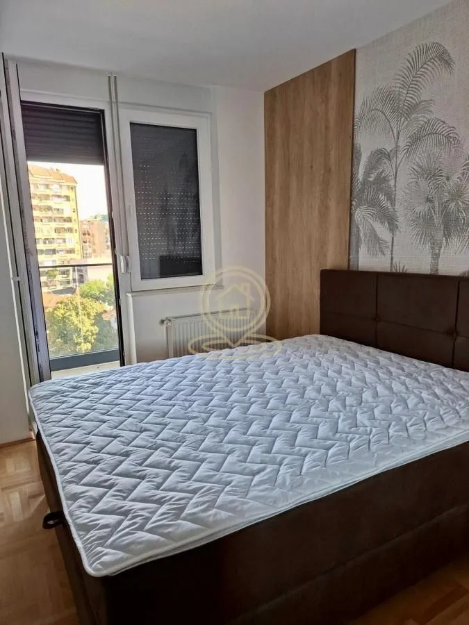 Nameštena spavaća soba sa bračnim krevetom i izlazom na balkon.