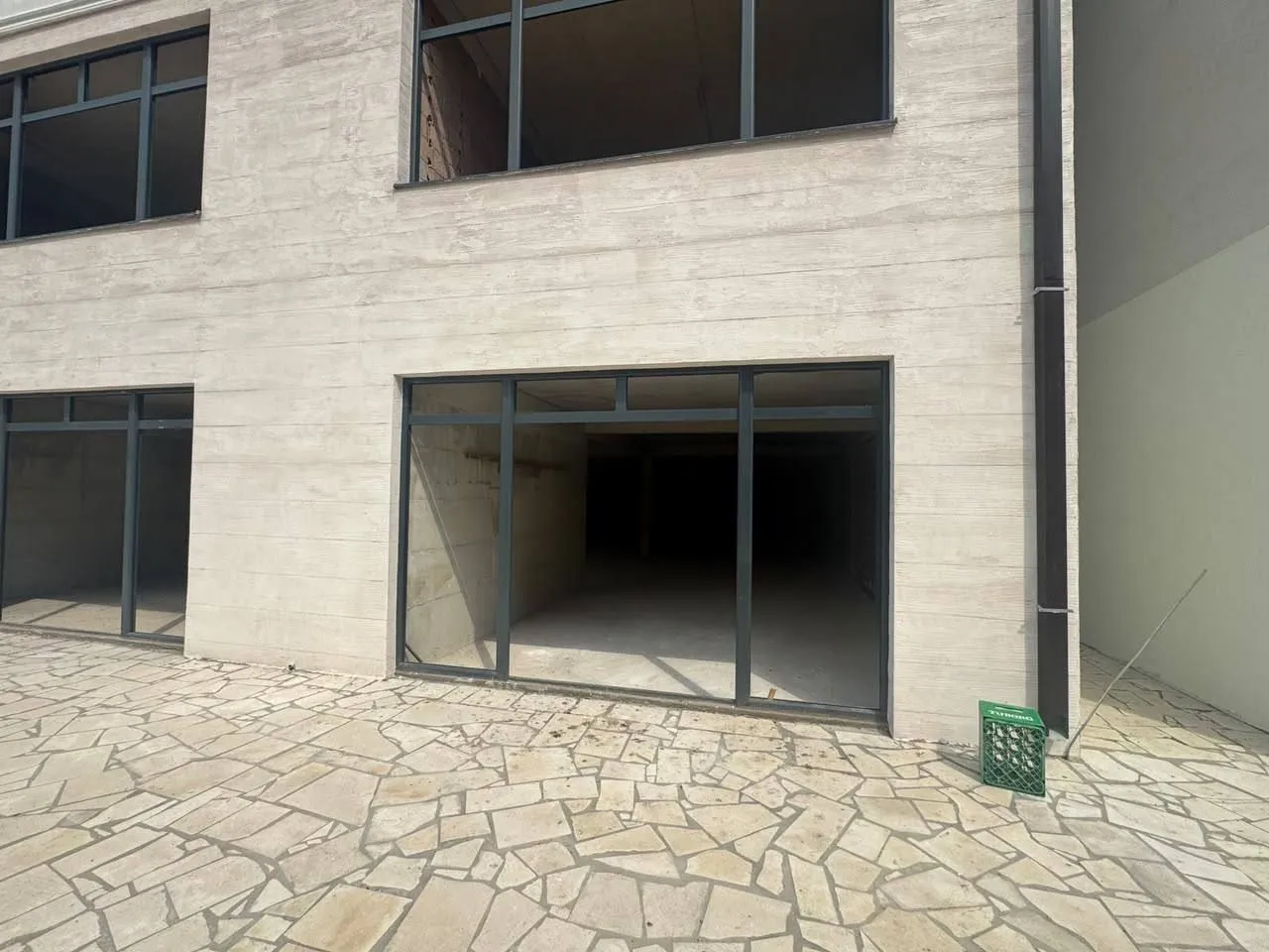 Exterior view of the building with a paved yard and large glass openings.