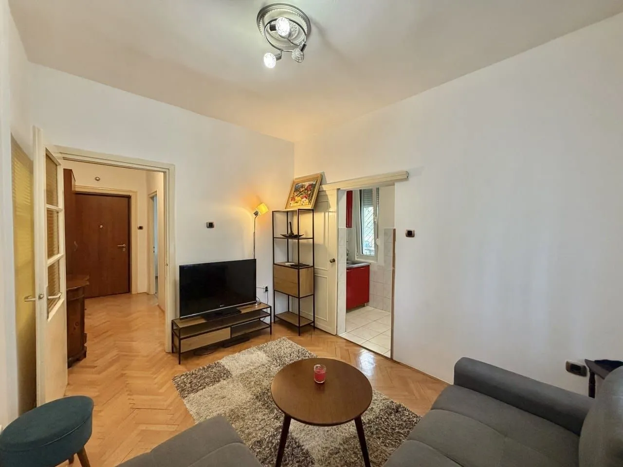 Living room with sofa, television, and a view into the kitchen and hallway.