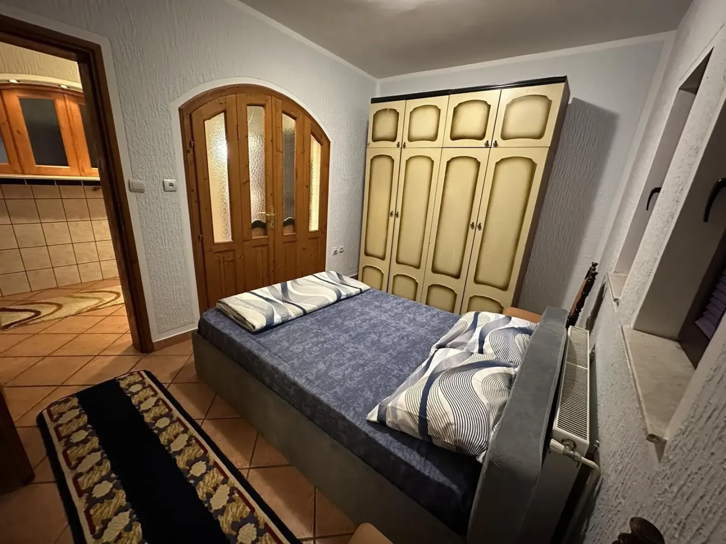 Spavaća soba sa bračnim krevetom, velikim ormarom i drvenim vratima.