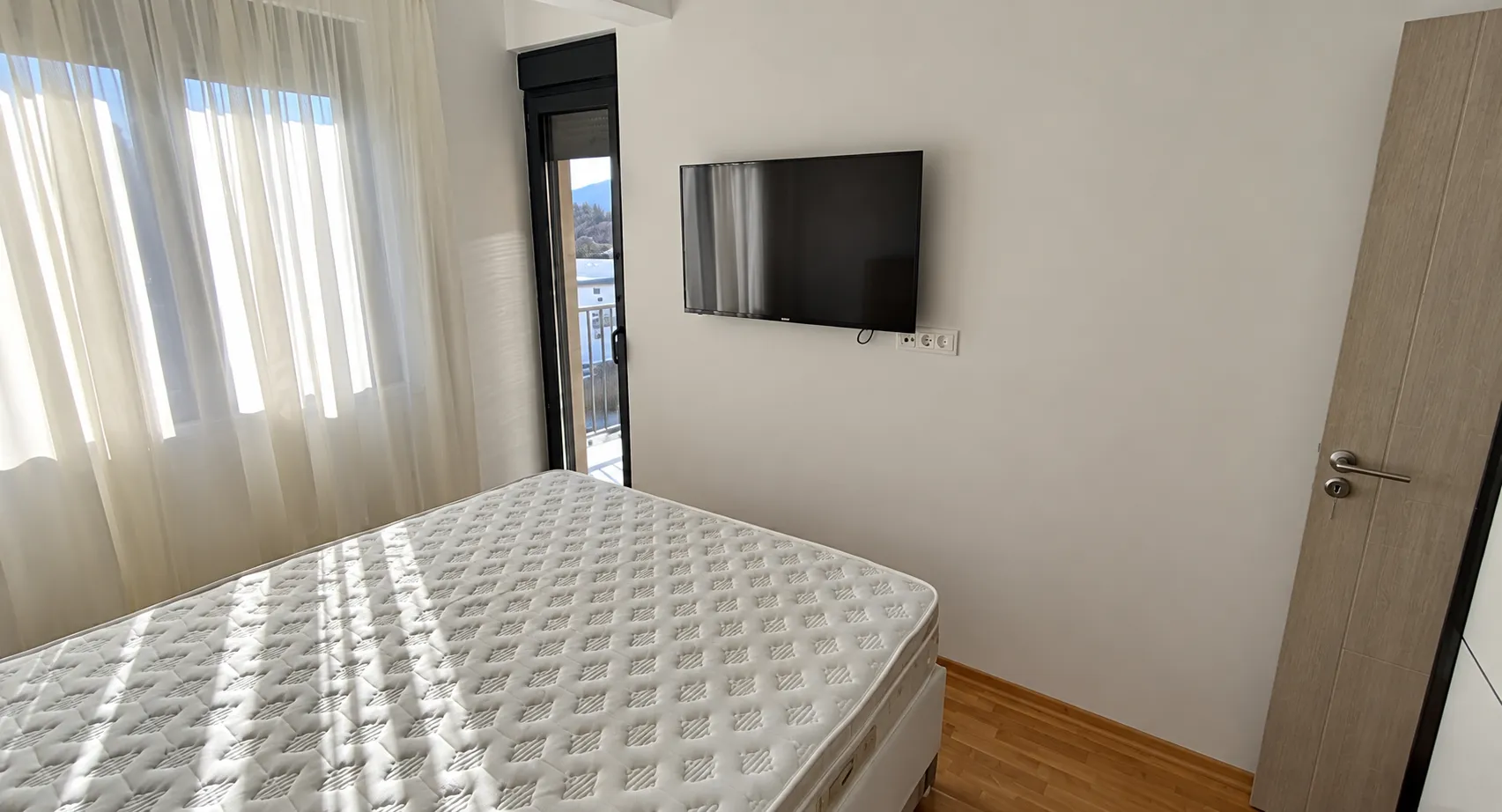 Bedroom with a bed, wall-mounted TV, and balcony access.