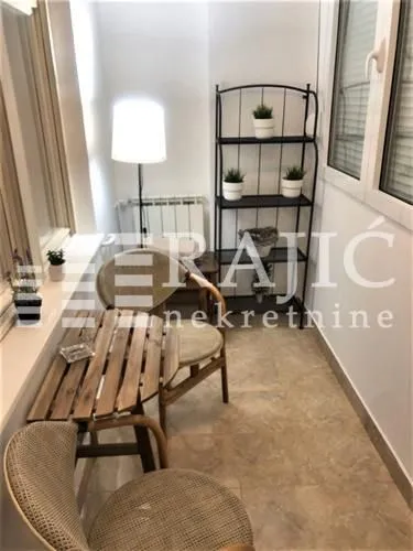 Enclosed balcony furnished with a small table, chairs, and a shelf with plants.