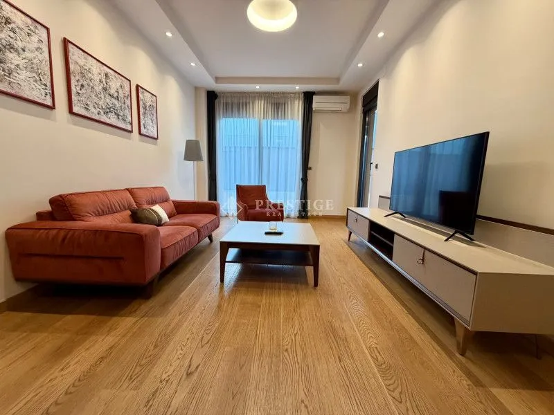 Modern and bright living room with a sofa, TV, and wooden flooring.