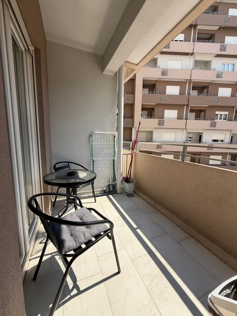 Small furnished balcony with a table and chairs and a view of surrounding buildings.