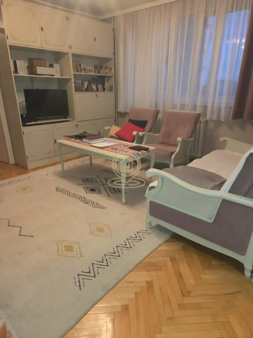 Dnevni boravak sa garniturom za sedenje, televizorom i velikim ormarom.