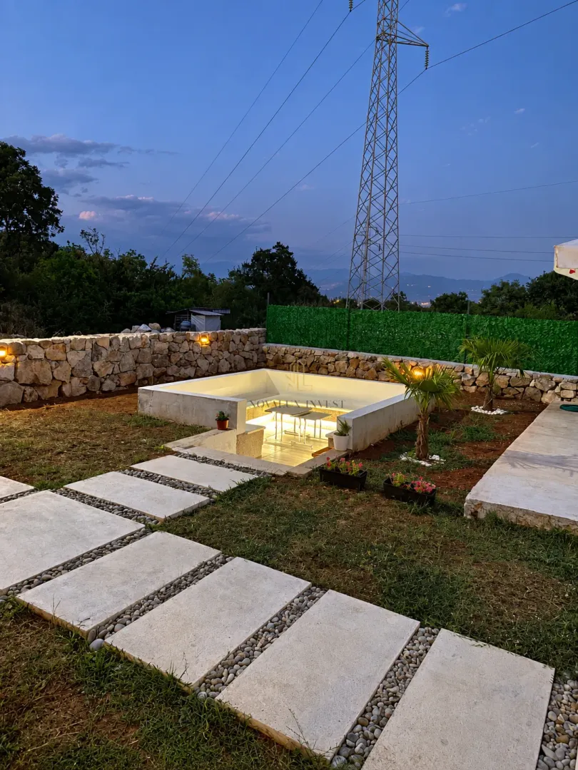 Landscaped yard with an illuminated seating area and a stone wall.