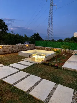 Landscaped yard with an illuminated seating area and a stone wall. - image 8