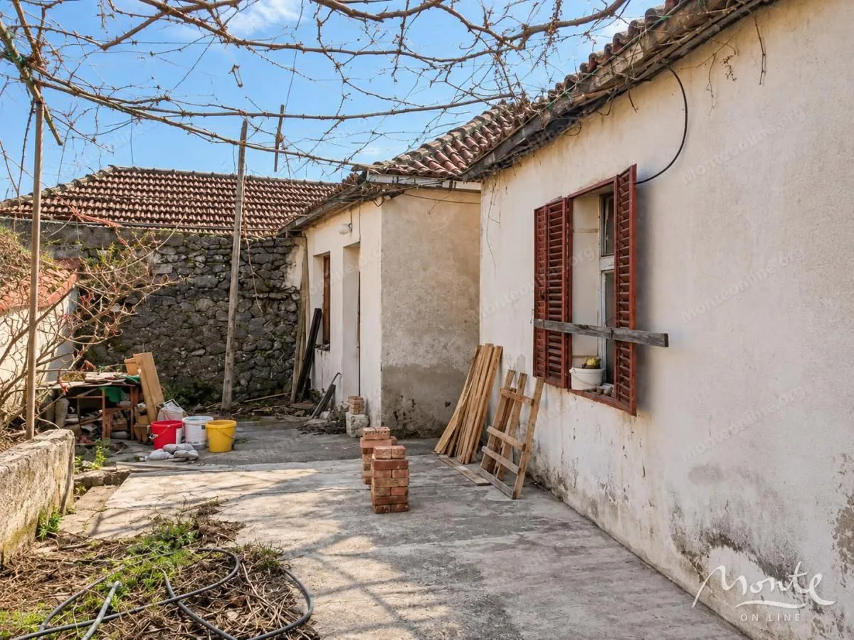 Pogled na dvorište i spoljašnjost starije kuće sa građevinskim materijalom.