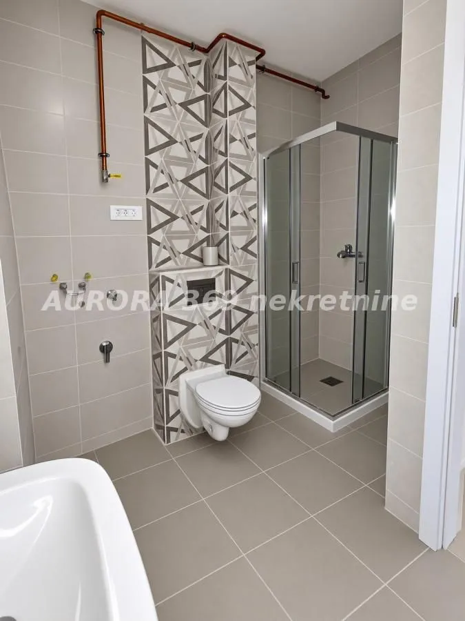 Moderno kupatilo sa tuš kabinom, WC šoljom i pločicama sa dezenom.