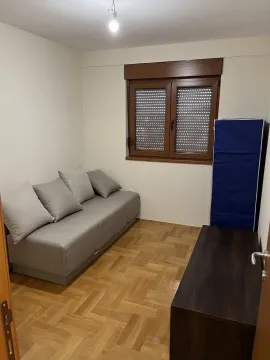 A simply furnished small room with a gray sofa and parquet flooring. - image 5