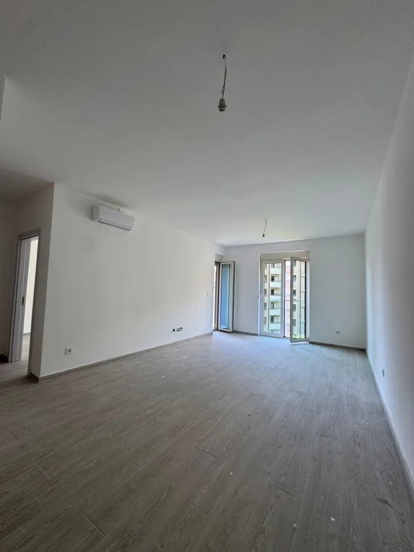 Prazna neopremljena prostorija sa bijelim zidovima, drvenim podom i izlazom na terasu.