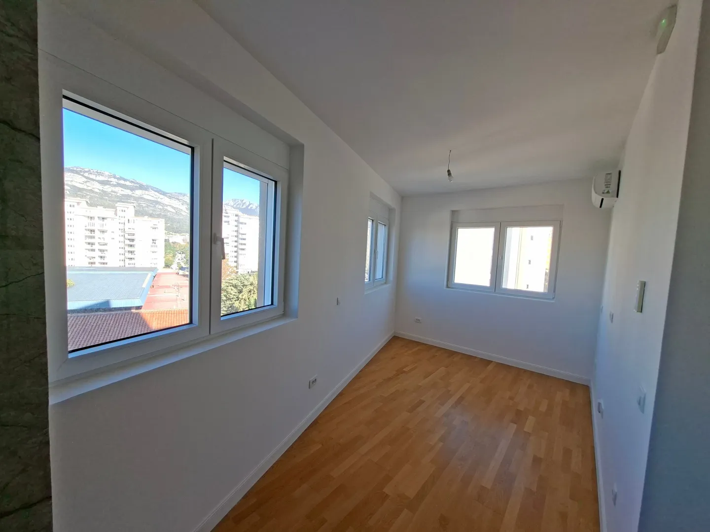 Empty room with white walls, parquet flooring, and a view through the windows.