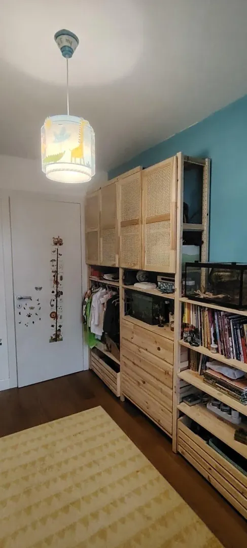 Children's room with a wooden wardrobe, shelves, and a rug on the floor.
