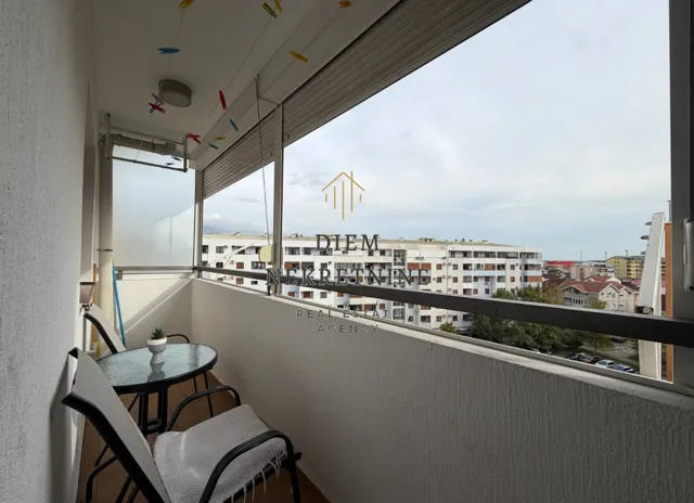 Zastakljeni balkon sa garniturom za sedenje i pogledom na grad.