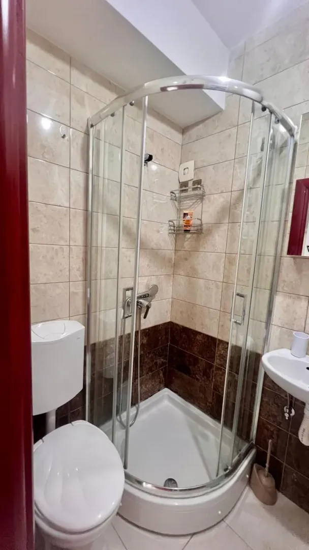 Small bathroom with a shower cabin, toilet, and washbasin tiled with ceramic tiles.