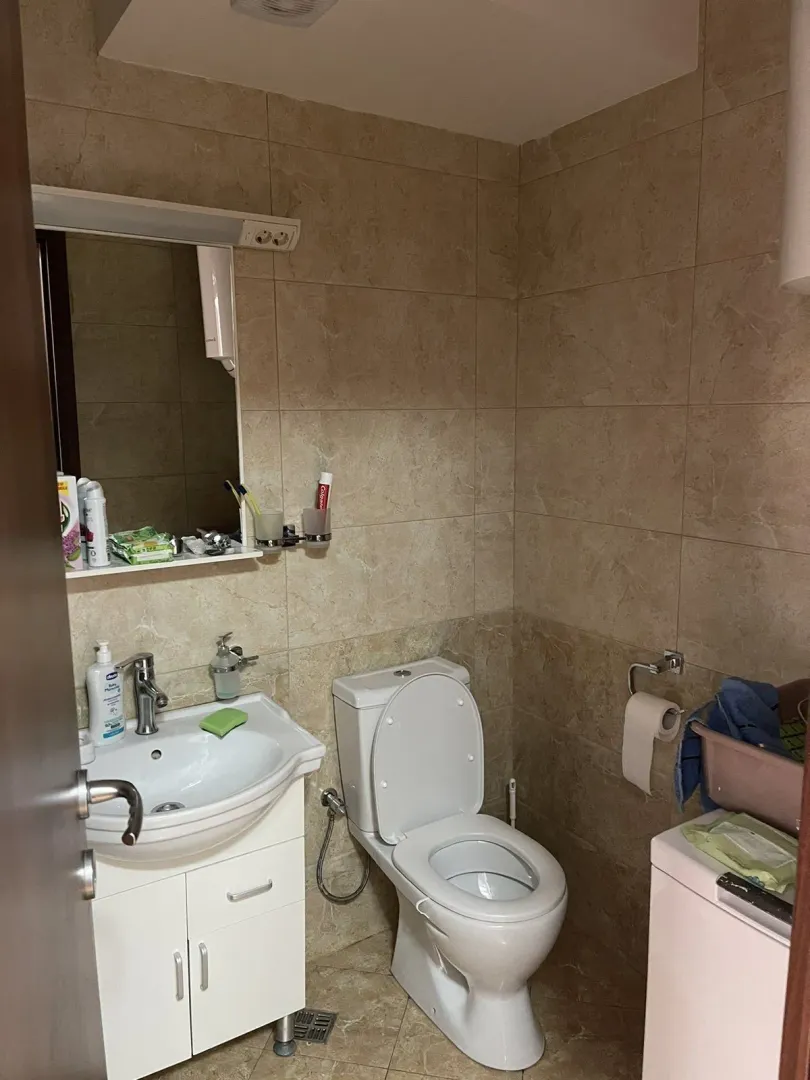 Jednostavno kupatilo sa bež pločicama, lavaboom i toaletom.