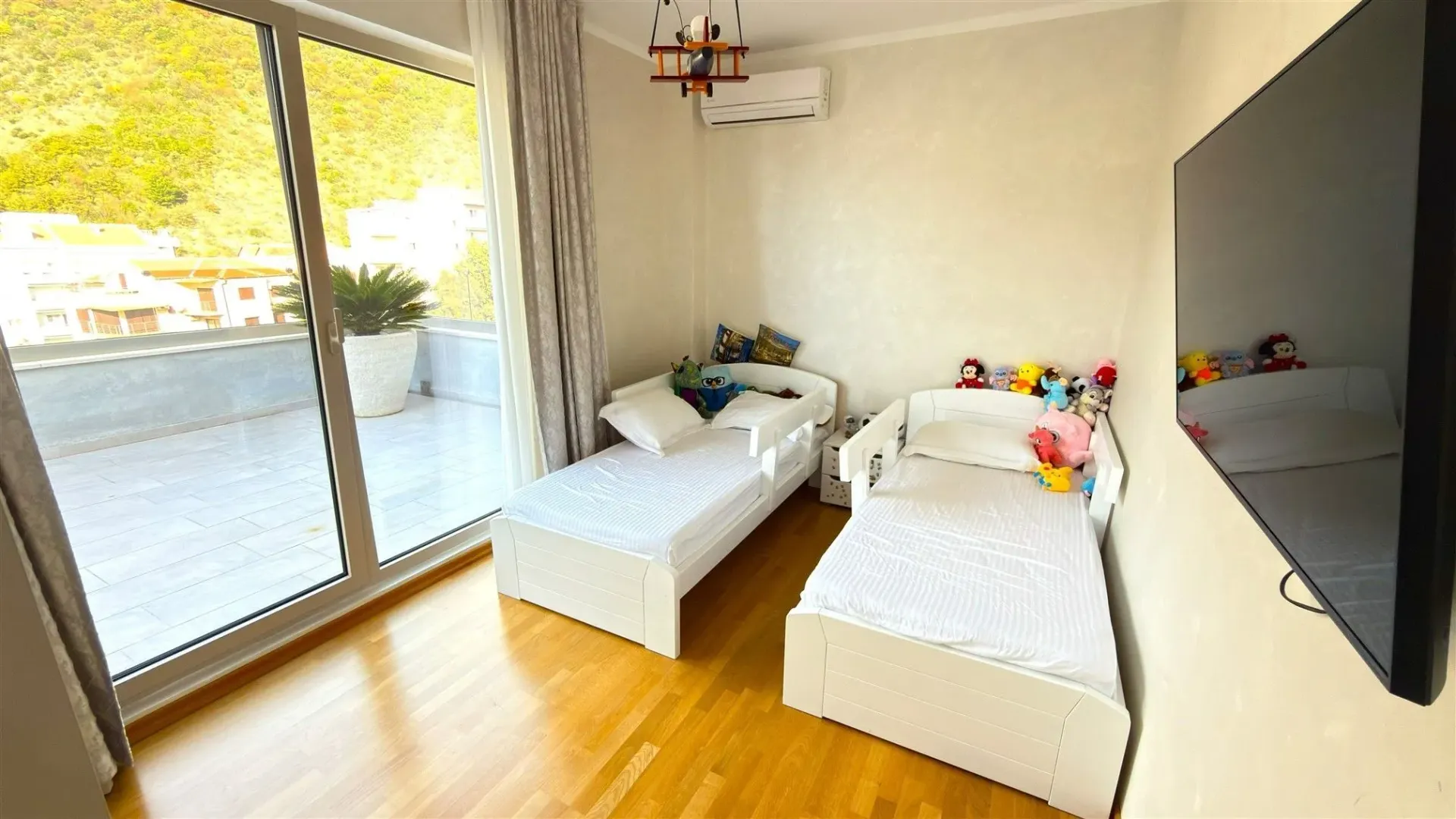Svijetla dječija soba sa dva kreveta za jednu osobu i izlazom na balkon.