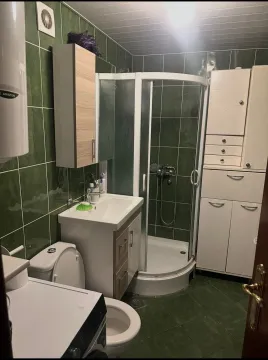 Kupatilo sa tuš kabinom, umivaonikom, WC šoljom i zelenim pločicama. - image 5