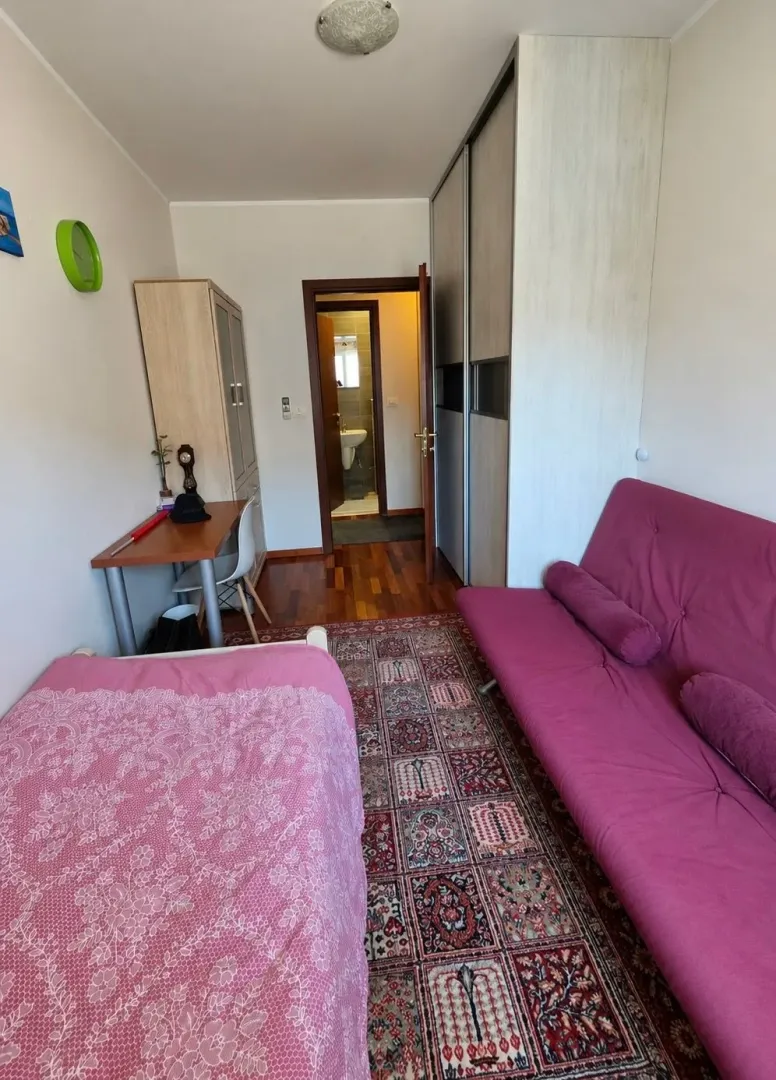Namještena spavaća soba sa krevetom, ljubičastom sofom, radnim stolom i plakarom.
