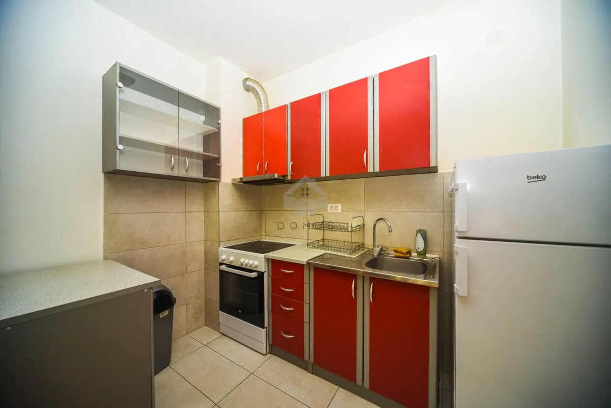 Small kitchen with red cabinets, stove, and refrigerator.