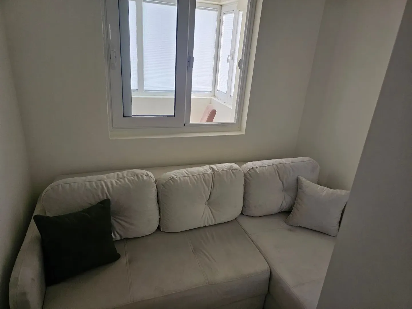 Ugaona garnitura u dnevnoj sobi pored prozora sa pogledom na balkon.