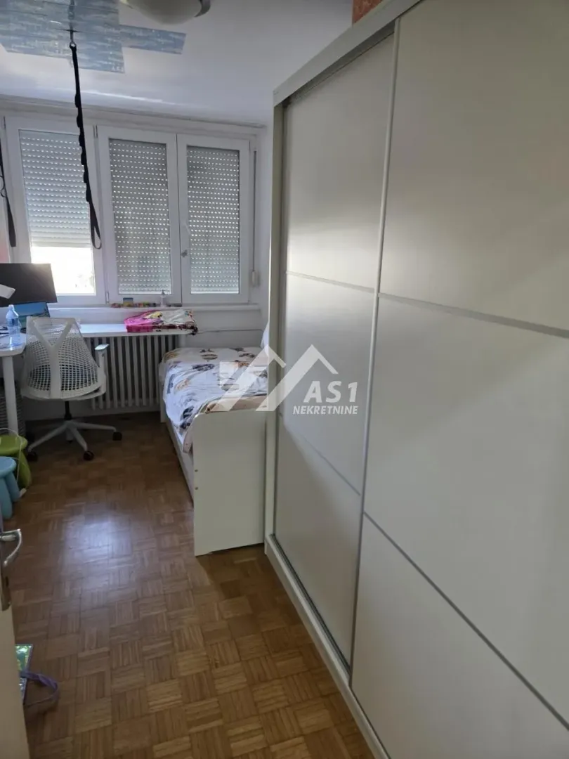 Dečja soba sa krevetom, radnim stolom i velikim ugradnim ormanom.
