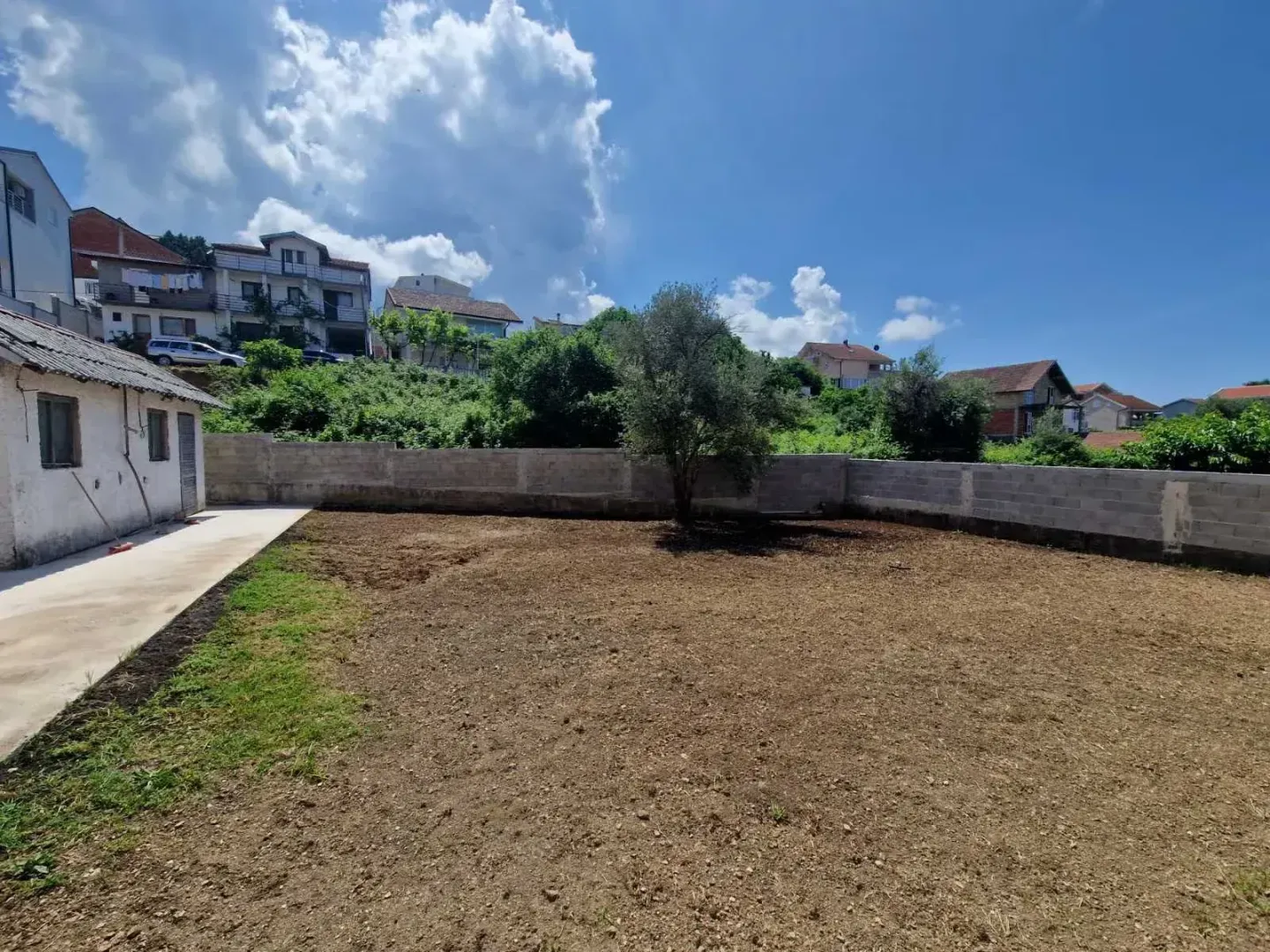 Ograđeno dvorište sa zemljištem i pogledom na okolne kuće.