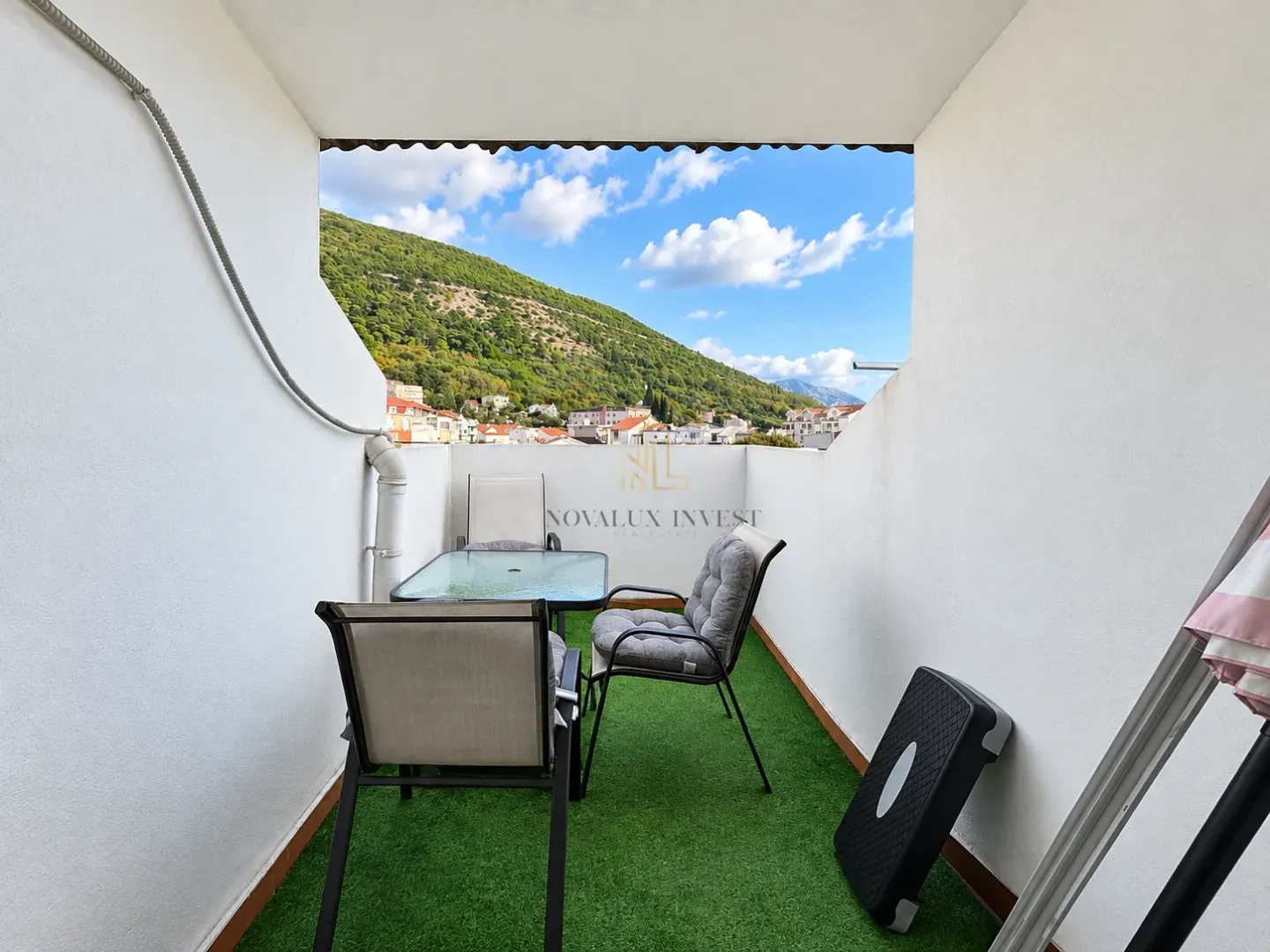 Namtještena terasa sa stolom, stolicama i vještačkom travom i pogledom na brdo.