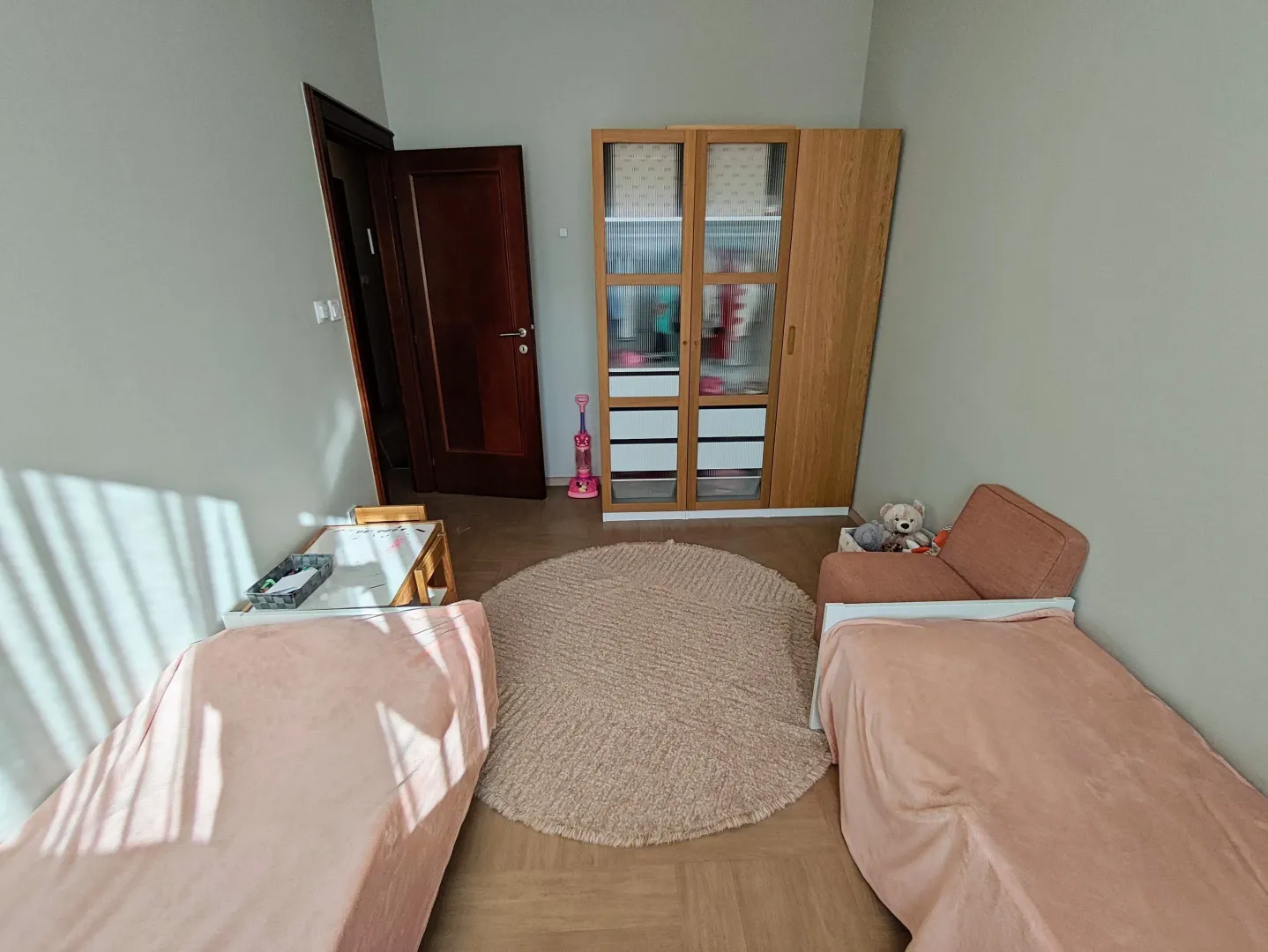 Dječija soba sa dva kreveta, ormarom i okruglim tepihom.