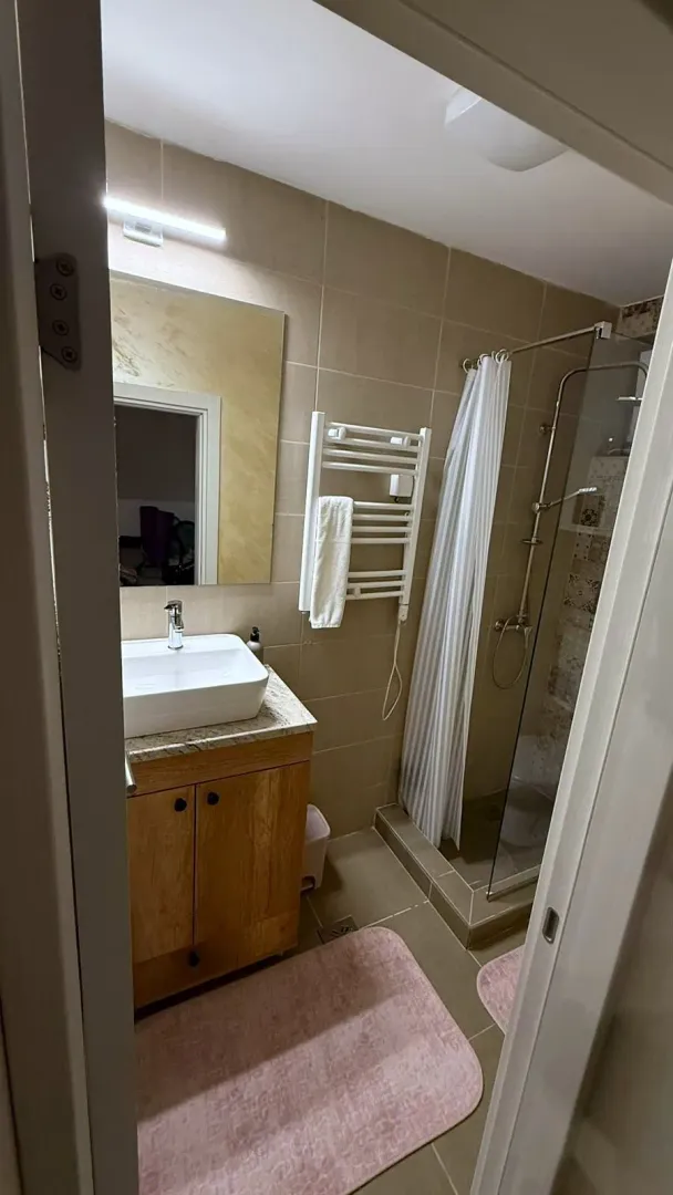 Manje kupatilo sa umivaonikom, drvenim ormarićem i tuš kabinom.