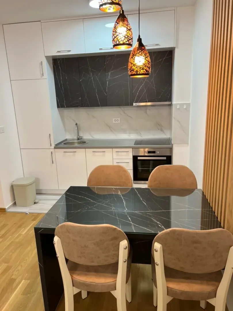 Svijetla kuhinja sa trpezarijskim stolom i modernim visećim svjetiljkama.