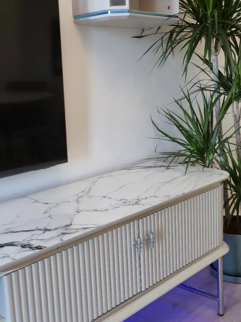 Detalj enterijera sa komodom i televizorom na zidu u dnevnoj sobi.