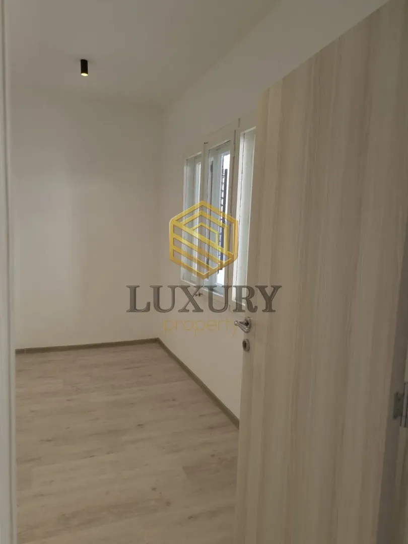 View of an empty room with light laminate flooring through an open door.