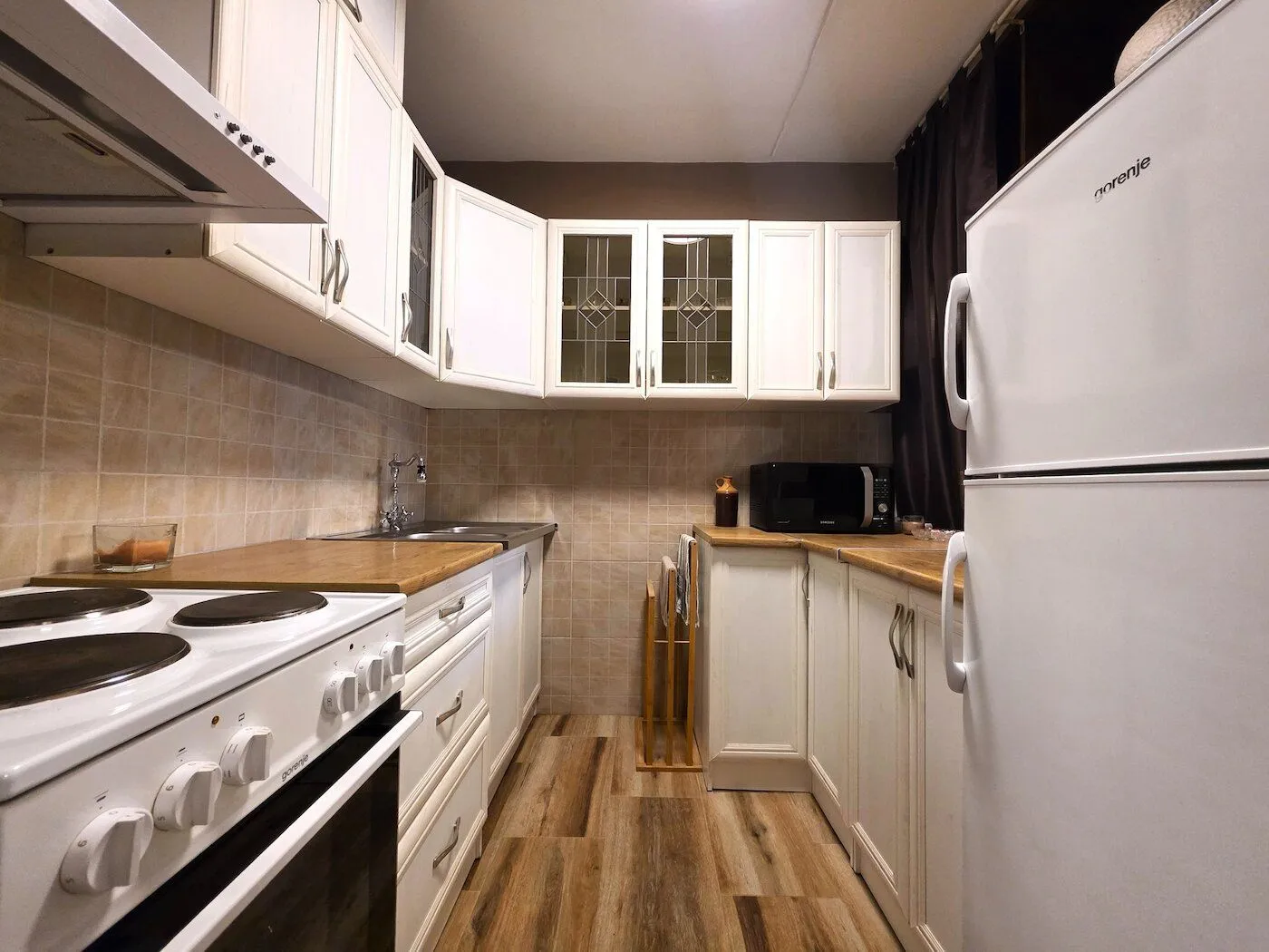 View of a furnished kitchen with white cabinets and a wooden countertop.
