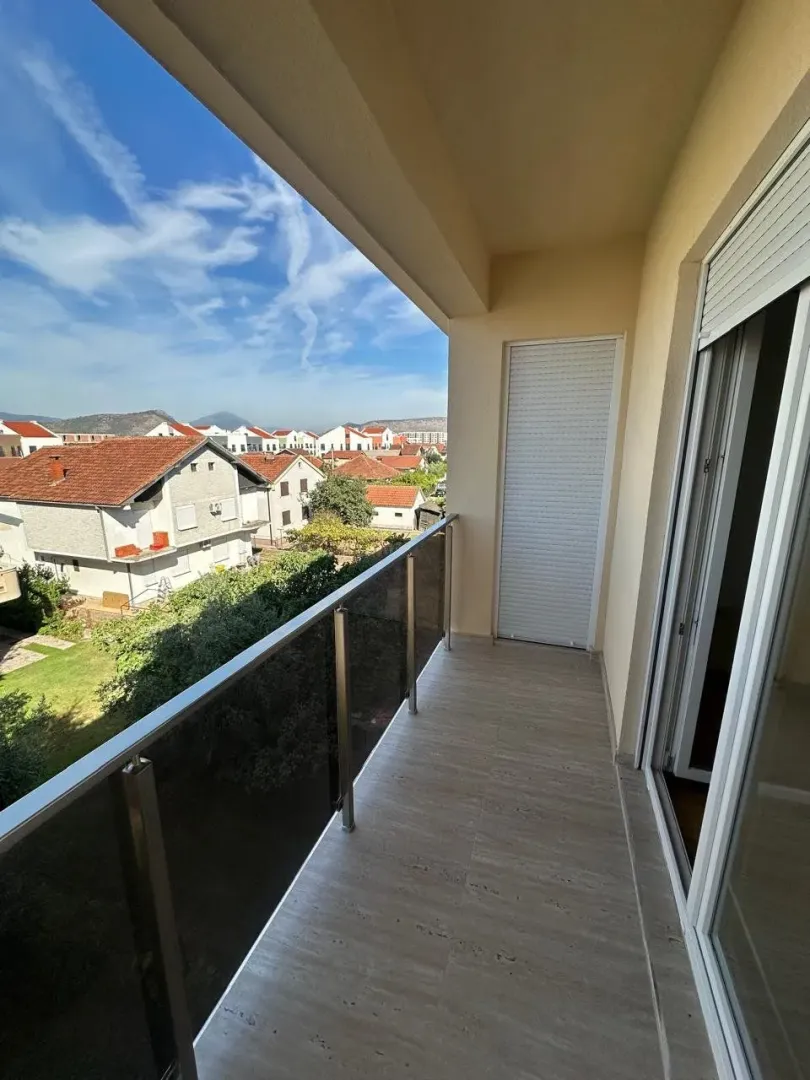 Covered balcony with a glass railing and a view of the neighborhood and surrounding hills.