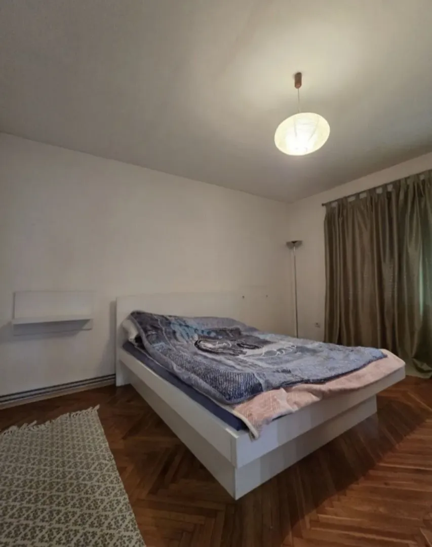 Spavaća soba sa bračnim krevetom, drvenim parketom i prozorom sa zavjesama.