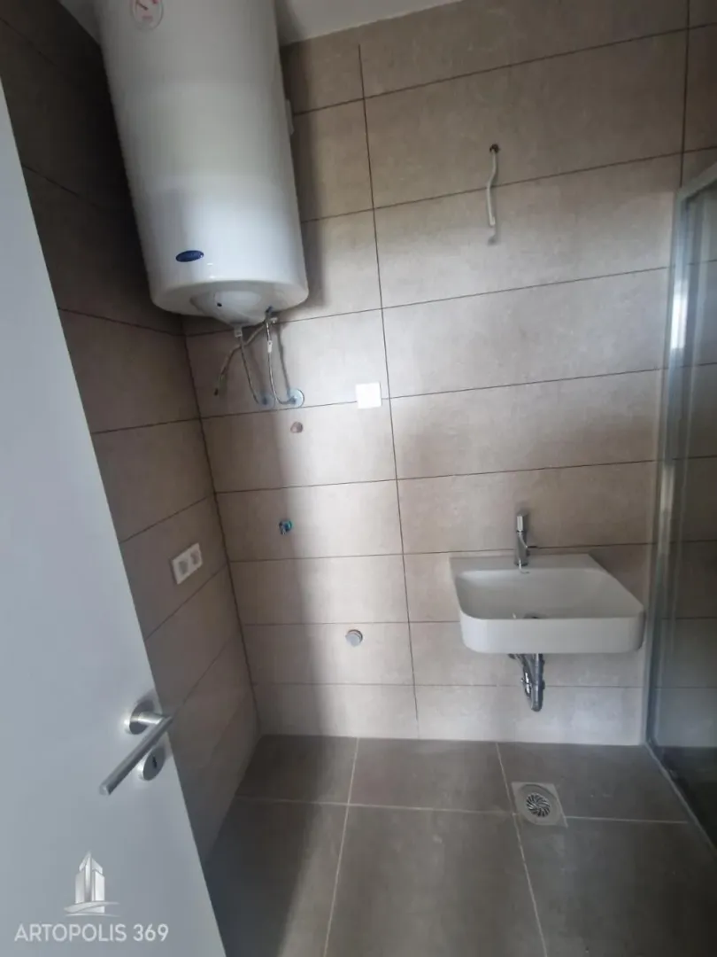 Bathroom with tiles, washbasin, shower cabin, and water heater.
