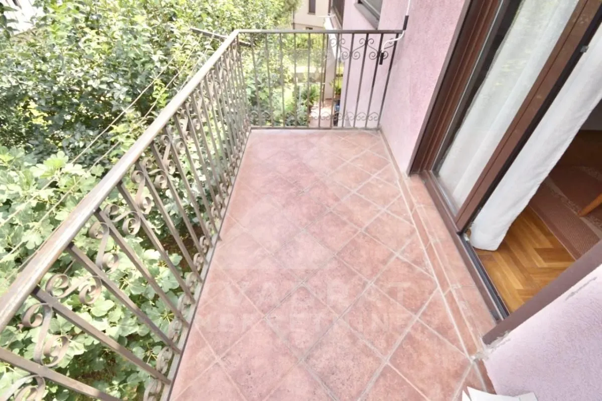 Balcony with tiled flooring and wrought iron railing surrounded by greenery.