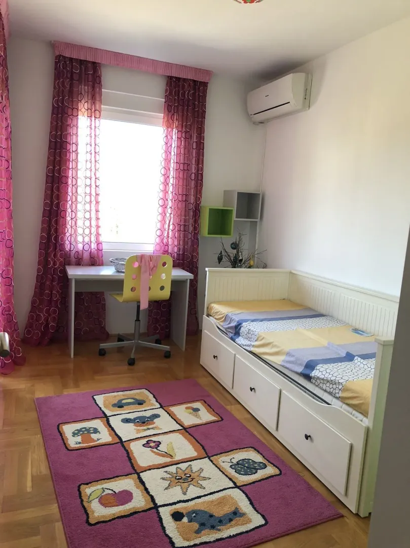 A bright children's bedroom with a bed, study desk, and a colorful rug.