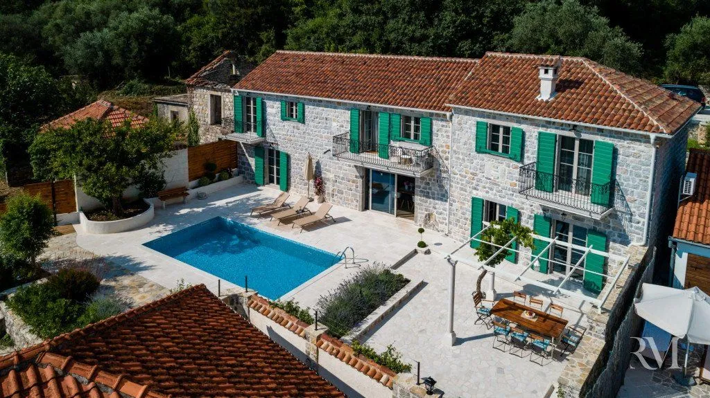 Aerial view of a stone house with a swimming pool and yard.