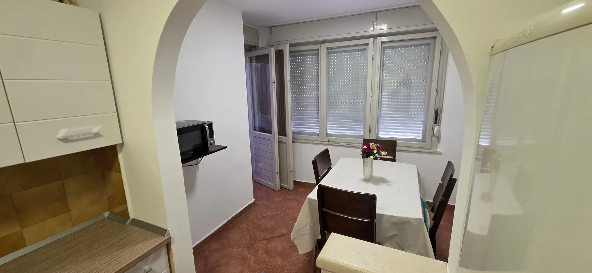 Smaller kitchen with a dining table and chairs, viewed through an archway.